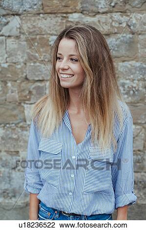 Stock Image - Portrait of young woman against stonewall. Fotosearch