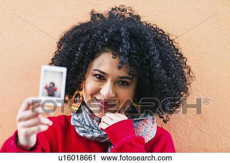 Stock Image - Portrait of young woman holding photograph of herself. Fotosearch