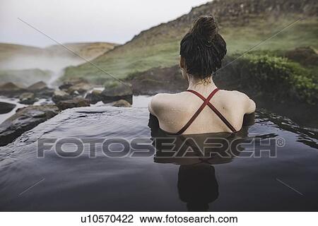 Stock Image - Rear view of woman in hot pool Iceland. Fotosearch