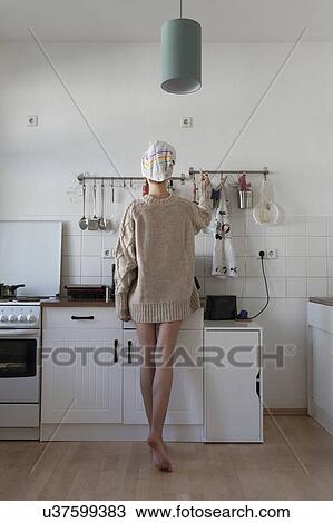 Stock Image - Rear view of young woman in apartment kitchen. Fotosearch