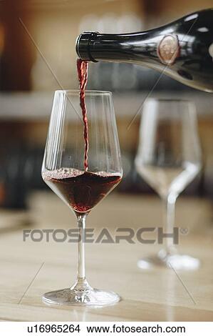 Picture - Red wine poured from bottle into wineglass. Fotosearch
