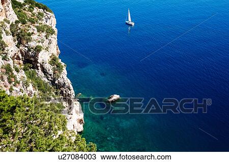 Stock Image - Scenic view of blue sea and yacht from cliff, high angle view, Alghero, Sardinia, Italy. Fotosearch