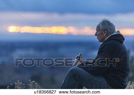 Seated man holding smart phone at sunset View Large Photo Image Stock Photo - Seated man holding smart phone at sunset. Fotosearch