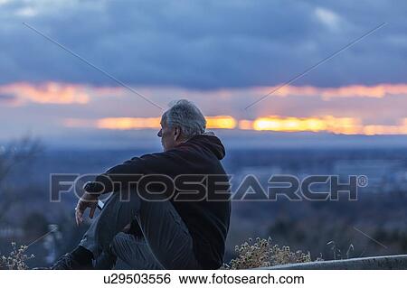 Seated man holding smart phone at sunset View Large Photo Image Stock Photograph - Seated man holding smart phone at sunset. Fotosearch