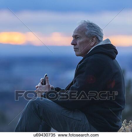 Seated man holding smart phone at sunset View Large Photo Image Stock Photography - Seated man holding smart phone at sunset. Fotosearch