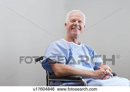 Stock Photograph - Senior man in hospital gown in wheelchair, smiling.. Fotosearch