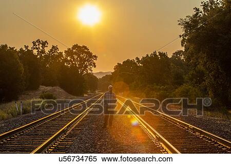 Stock Photography - Senior man standing between railroad tracks at sunset. Fotosearch
