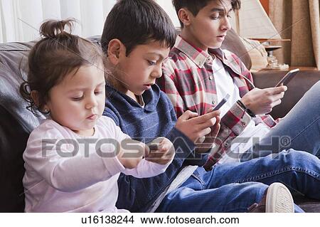 Picture - Siblings using smart phones on sofa. Fotosearch
