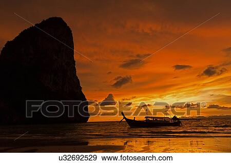 Stock Photo - Silhouette of boat by cliff at sunset in West Railay, Thailand. Fotosearch