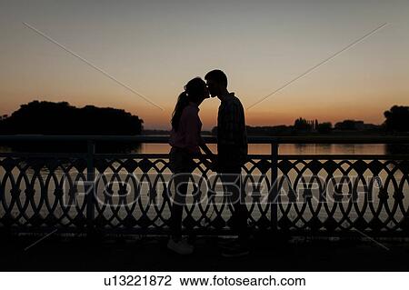 Silhouettes of young couple kissing at sunset View Large Photo Image Stock Image - Silhouettes of young couple kissing at sunset. Fotosearch