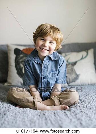 Picture - Smiling boy sitting on bed. Fotosearch