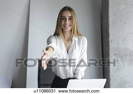 Stock Image - Smiling businesswoman reaching for handshake. Fotosearch