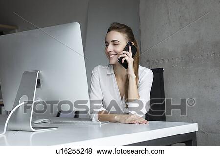 Smiling businesswoman taking phone call at desk View Large Photo Image Stock Photo - Smiling businesswoman taking phone call at desk. Fotosearch