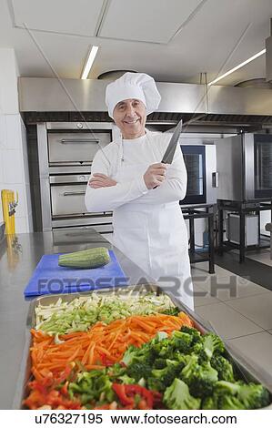 Stock Photography - Smiling chef holding kitchen knife by raw vegetables. Fotosearch