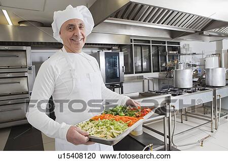 Stock Image - Smiling chef holding tray of vegetables. Fotosearch