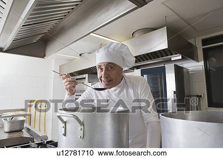 Stock Image - Smiling chef tasting food from pot. Fotosearch