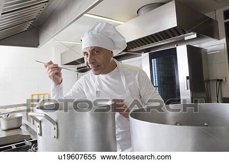 Stock Photography - Smiling chef tasting food from pot. Fotosearch