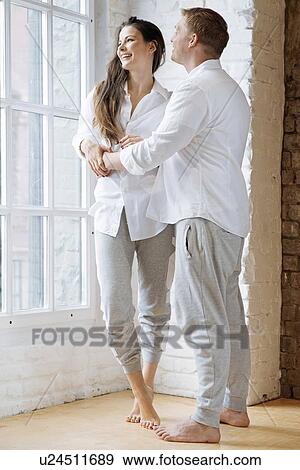 Stock Photo - Smiling couple embracing by window. Fotosearch