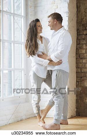 Stock Photography - Smiling couple embracing by window. Fotosearch