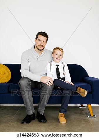 Stock Photo - Smiling father and son sitting on sofa. Fotosearch