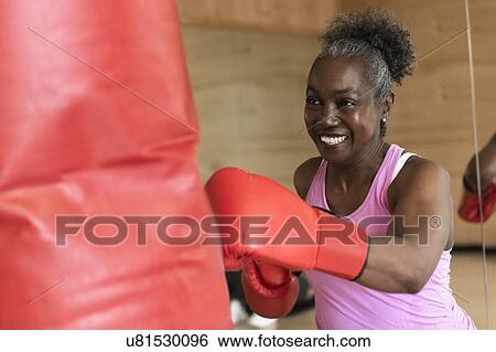 Stock Photograph - Smiling mature woman boxing with punching bag. Fotosearch