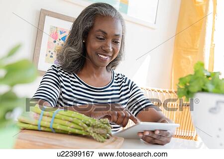 Stock Photo - Smiling mature woman looking at digital tablet. Fotosearch