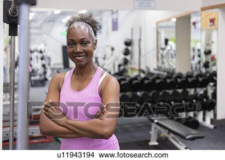 Picture - Smiling mature woman with arms crossed in gym. Fotosearch