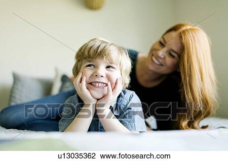 Stock Image - Smiling mother and son lying on bed. Fotosearch