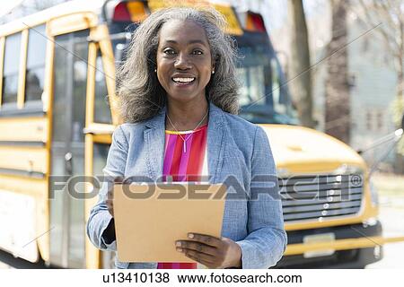 Smiling teacher with clipboard by school bus View Large Photo Image Stock Photo - Smiling teacher with clipboard by school bus. Fotosearch