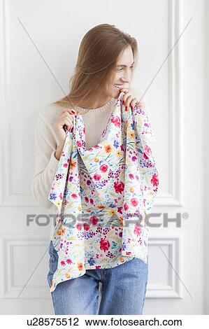 Stock Image - Smiling woman holding floral pattern fabric. Fotosearch