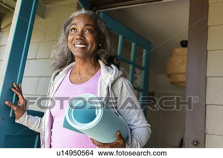 Picture - Smiling woman with yoga mat front door. Fotosearch