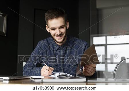 Stock Image - Smiling young businessman writing in note pad. Fotosearch