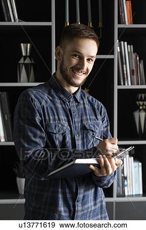 Smiling young businessman writing in note pad View Large Photo Image Stock Photo - Smiling young businessman writing in note pad. Fotosearch