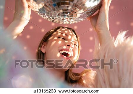 Stock Image - Smiling young woman holding mirror ball. Fotosearch
