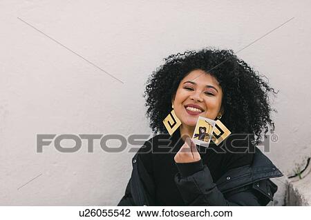 Stock Image - Smiling young woman holding photograph of herself. Fotosearch