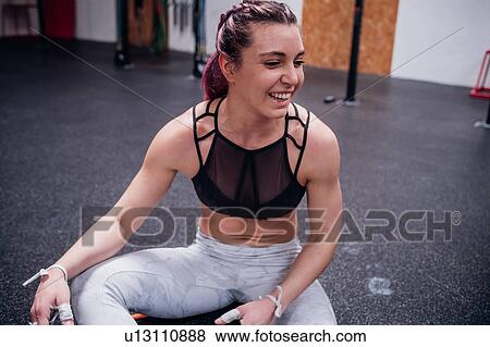 Stock Photo - Smiling young woman training, sitting on gym floor taking a break. Fotosearch