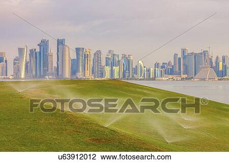 Stock Image - Sprinkler system on lawn by skyline of Doha, Qatar. Fotosearch