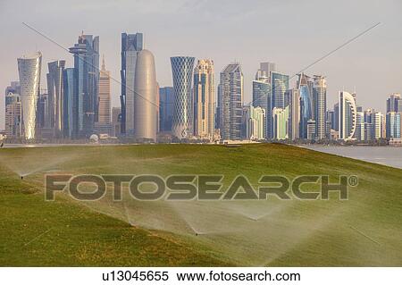 Stock Photography - Sprinkler system on lawn by skyline of Doha, Qatar. Fotosearch