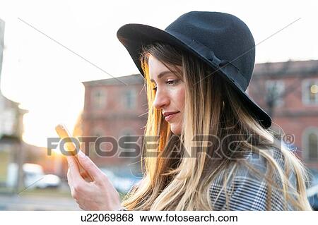 Stock Photo - Stylish young woman with long blond hair looking at smartphone on city street. Fotosearch