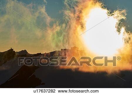 Stock Image - Sun behind veil of clouds over mountain range, Saas-Fee, Valais, Switzerland. Fotosearch