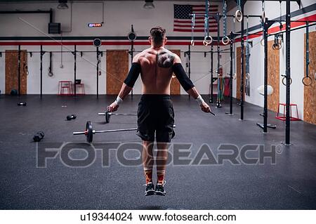 Picture - Tattooed young man training, skipping in gym, rear view. Fotosearch