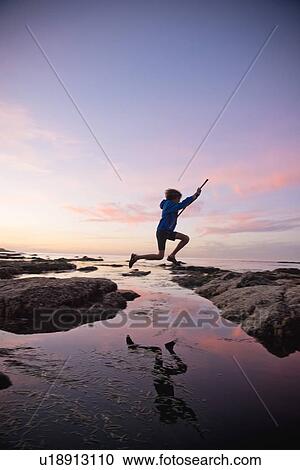 Stock Image - Teenage boy jumping between rocks of tide pool in La Jolla, California. Fotosearch