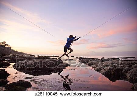 Stock Photography - Teenage boy jumping between rocks of tide pool in La Jolla, California. Fotosearch