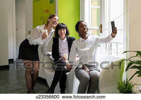 Three female business creatives taking a break and taking smartphone selfie in office View Large Photo Image Stock Image - Three female business creatives taking a break and taking smartphone selfie in office. Fotosearch