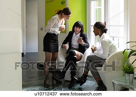 Three female business creatives taking a break and looking at smartphone in office View Large Photo Image Stock Photo - Three female business creatives taking a break and looking at smartphone in office. Fotosearch