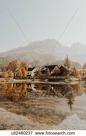 Stock Photo - Traditional houses on lakeside below misty mountain landscape, Admont, Styria, Austria. Fotosearch