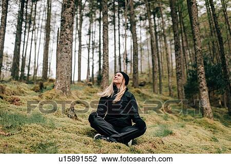 Stock Image - Trekker sitting cross-legged in forest, Trossachs National Park, Canada. Fotosearch