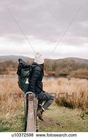 Stock Photo - Trekker sitting on fence by Loch Lomond, Trossachs National Park, Canada. Fotosearch