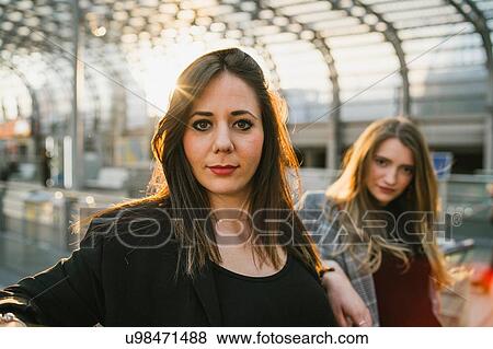 Stock Photo - Two confident young women in sunlit train station, portrait. Fotosearch