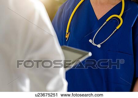 Two female junior doctors using digital tablet in hospital, over shoulder close up View Large Photo Image Stock Image - Two female junior doctors using digital tablet in hospital, over shoulder close up. Fotosearch